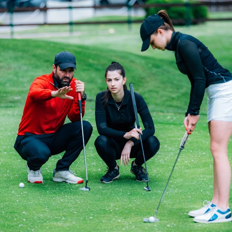 Golf putting lesson, two young female golfers practicing putting with golf instructor