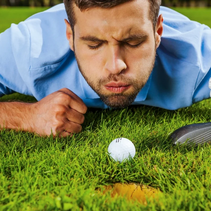 Close-up of young golfer blowing at the ball while lying near the hole