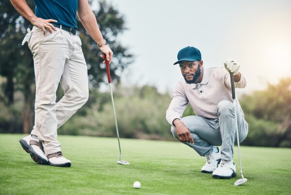 Two golfers assess a putt on the green, demonstrating smart decision-making and course management strategy during a round.