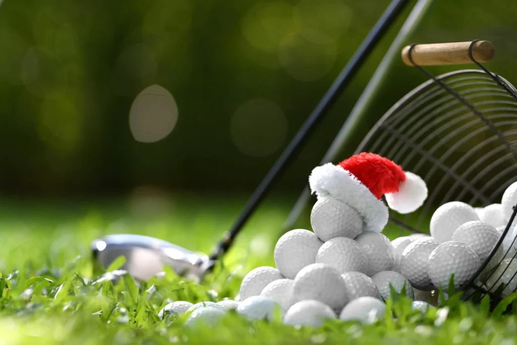 Golf balls on the grass with a Santa hat on top beside a club, highlighting a festive twist on winter golf.