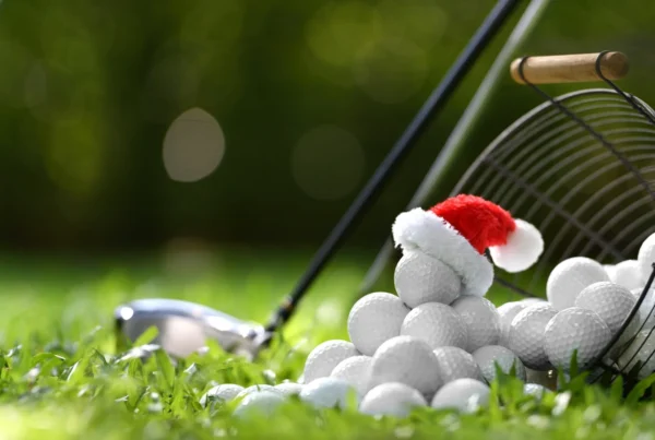 Golf balls on the grass with a Santa hat on top beside a club, highlighting a festive twist on winter golf.
