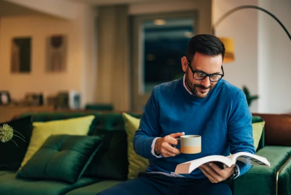 Cozy rainy-day reading setup with an open golf book on a tray beside a lit candle and a cup of coffee.