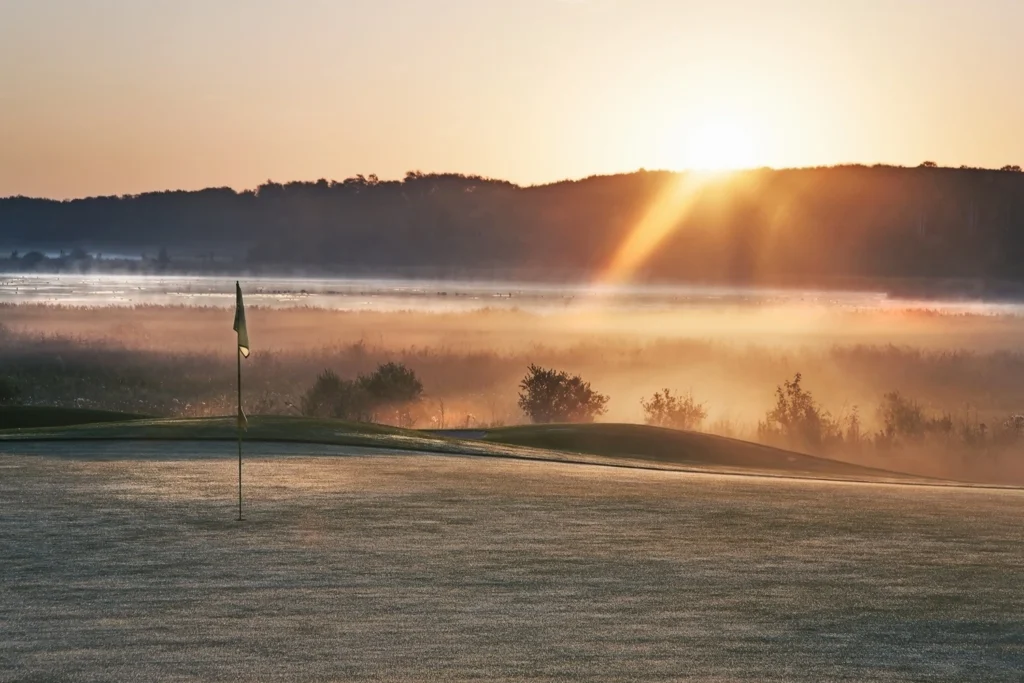 Winter golf green covered in frost at dawn, with sunlight and fog in the background
