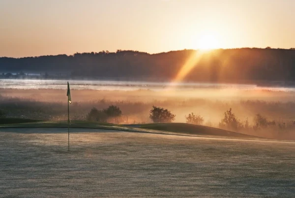 Winter golf green covered in frost at dawn, with sunlight and fog in the background