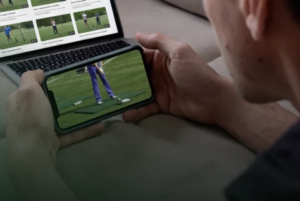 Golfer watching online golf swing tips on his phone and laptop at home